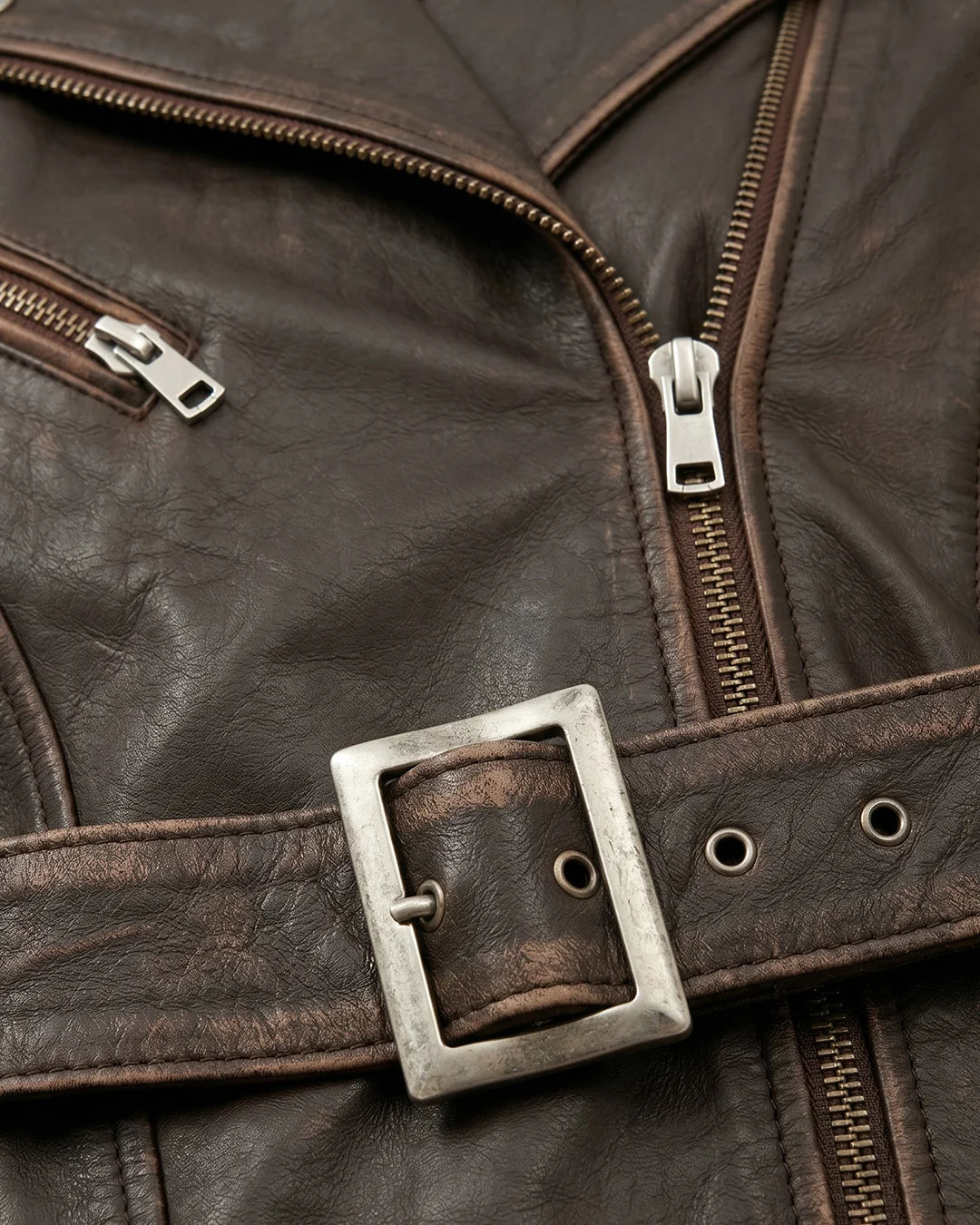 Close-up of a brown leather jacket with zippers and a belt buckle.