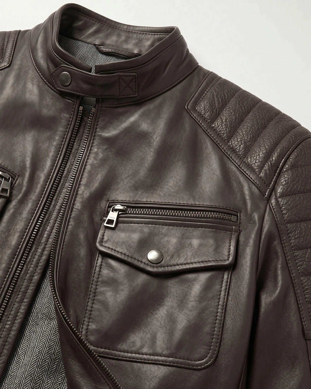 Close-up of a brown leather jacket with a pocket and zipper on a light gray background