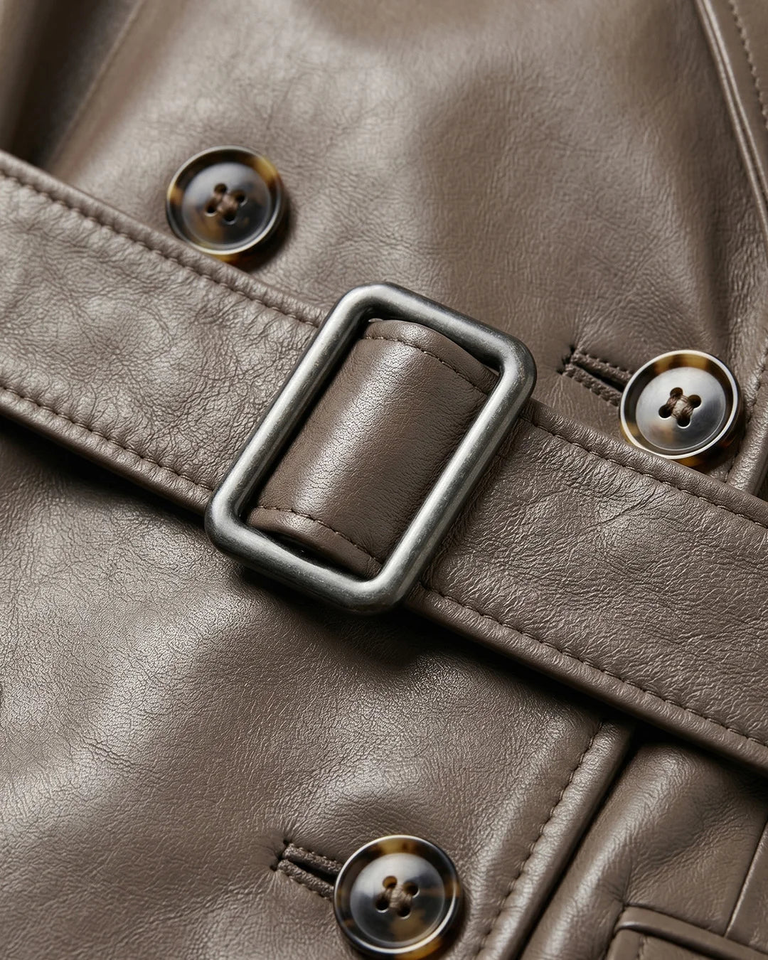 Close-up of a brown leather jacket with buttons and a buckle.