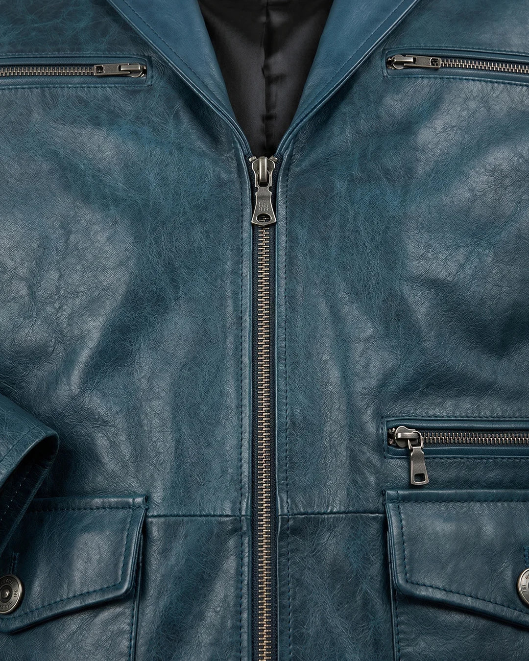 Close-up of a blue leather jacket with zippers and buttons.