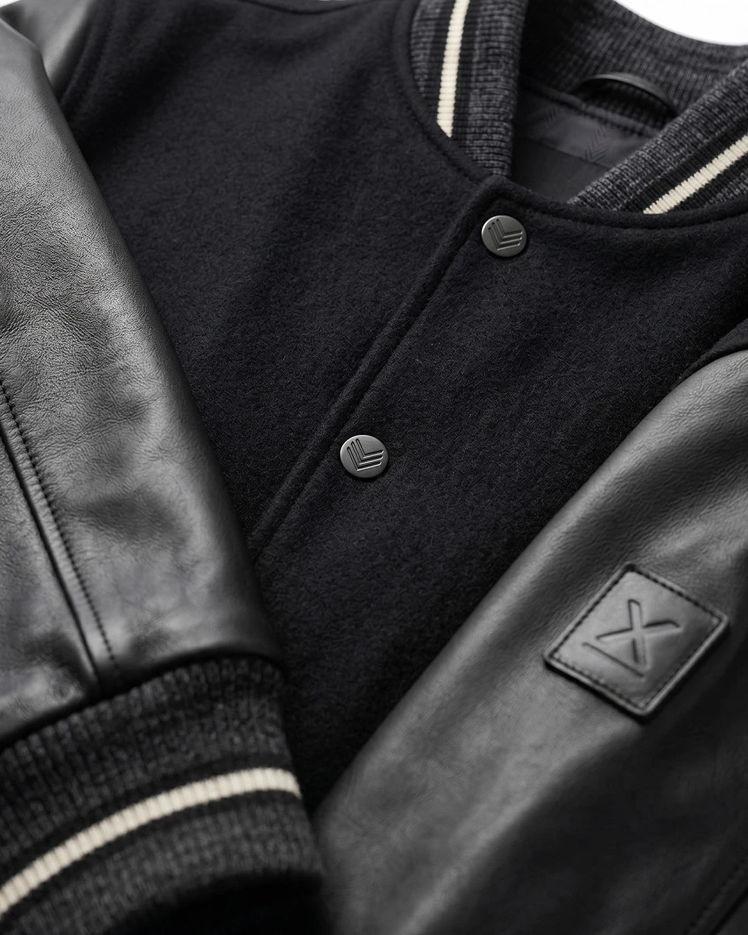Black varsity jacket with leather sleeves and a brand logo on a white background