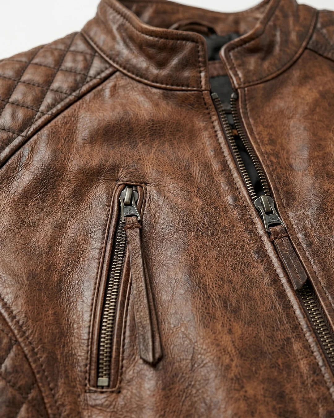 Close-up of a brown leather jacket with quilted details and zippers.