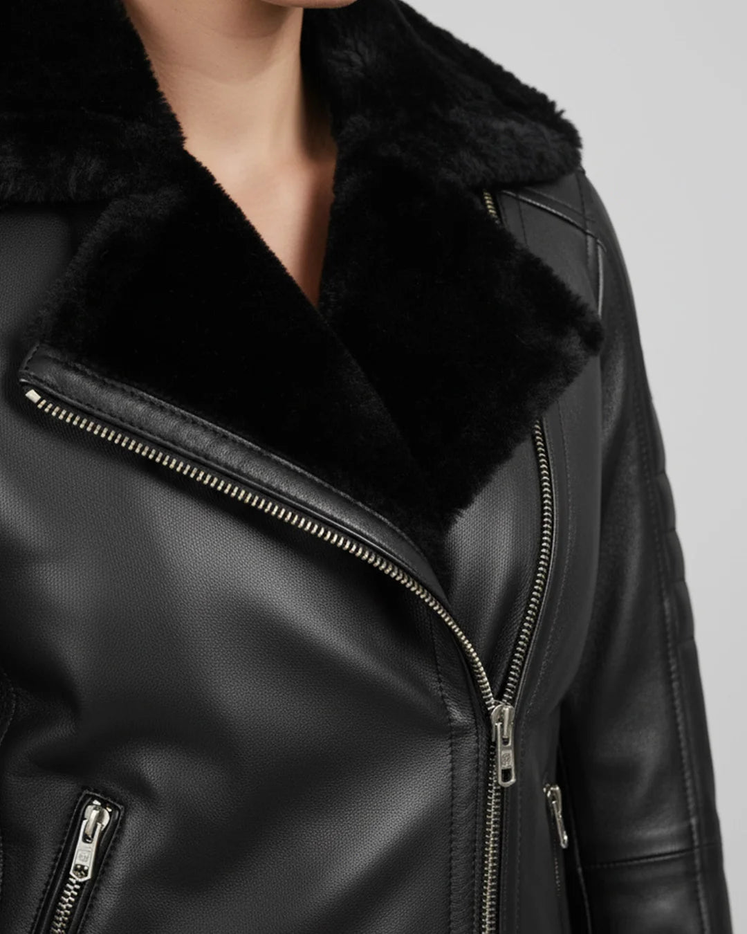 Close-up of a black leather jacket with fur collar on a neutral background